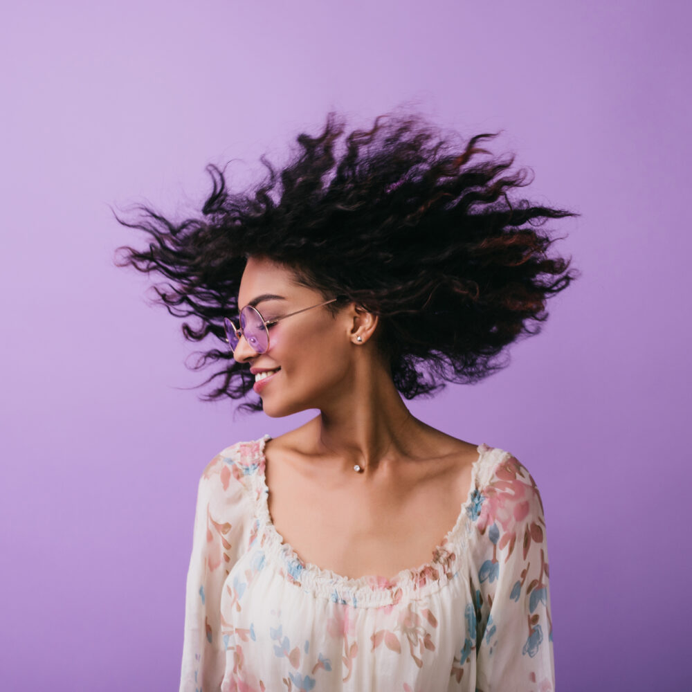 Studio photo of inspired african lady dancing with eyes closed. Indoor portrait of relaxed black girl isolated on purple background.